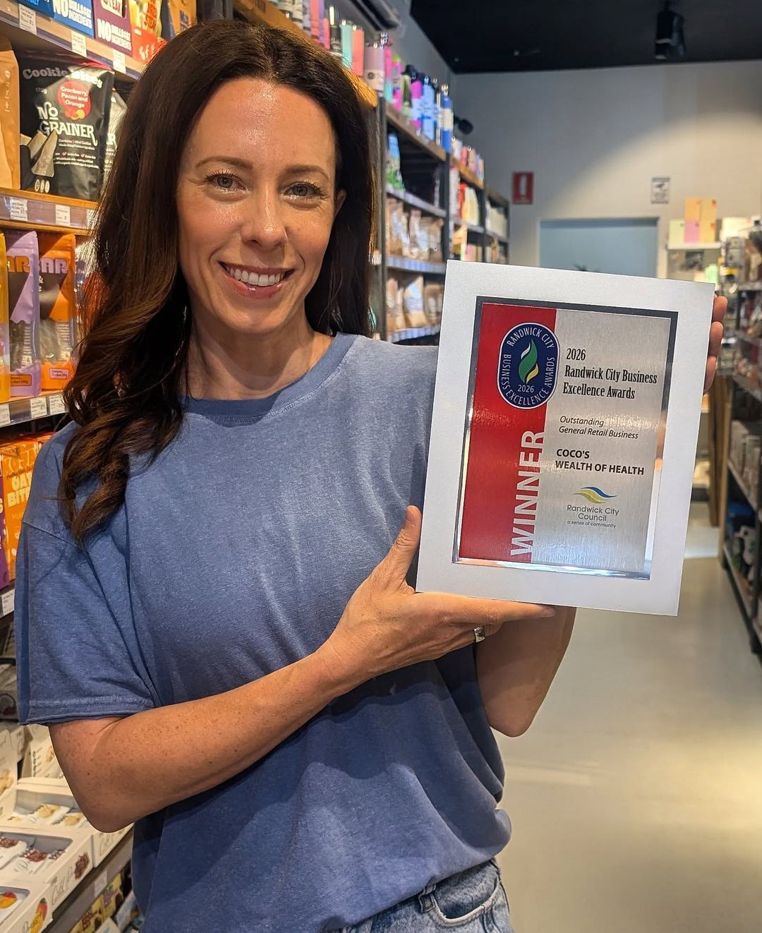 Coco holding the 2026 Randwick City Business Excellence Award for Outstanding General Retail Business, in store at Coco’s Wealth of Health